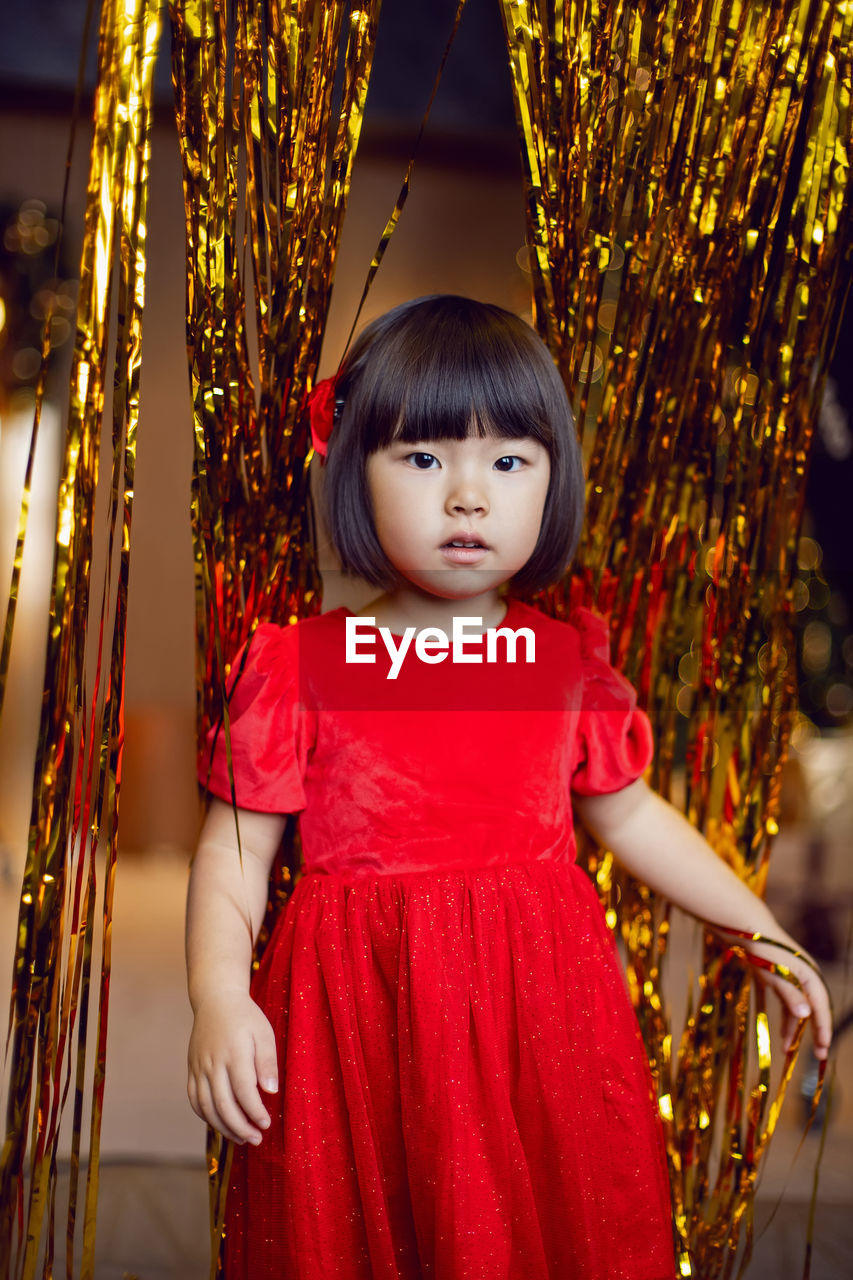 Portrait of a beautiful korean baby girl in a red dress at christmas with a gold decoration