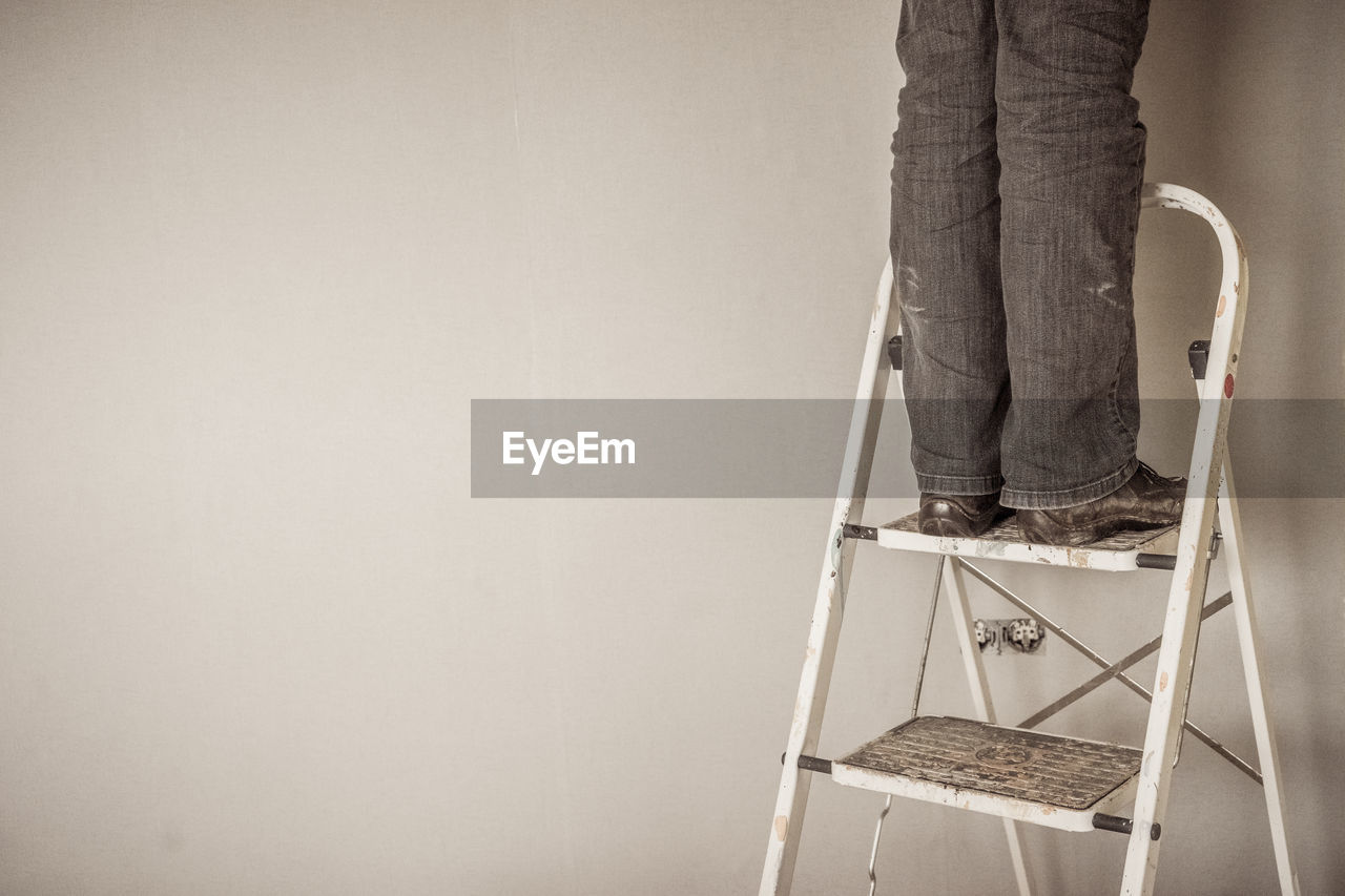 Low section of man standing on ladder against wall