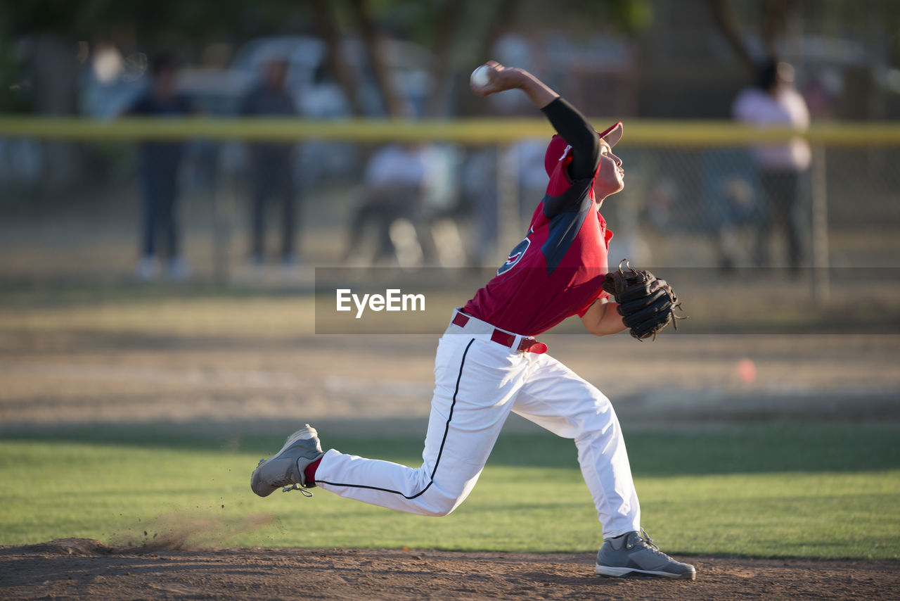 Teen baseball player pitching in red uniform in wind up on the mound