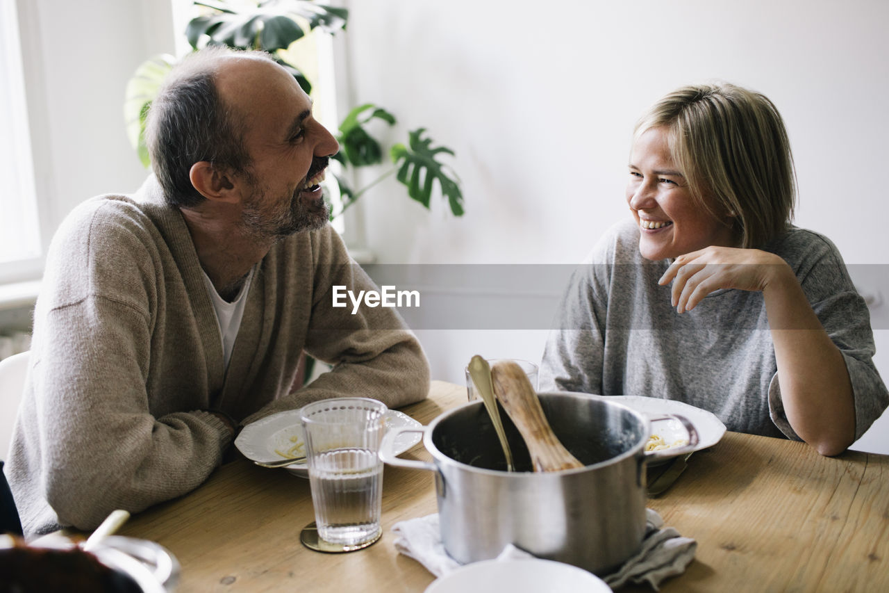 Happy mature couple talking to each other sitting at dining table in home