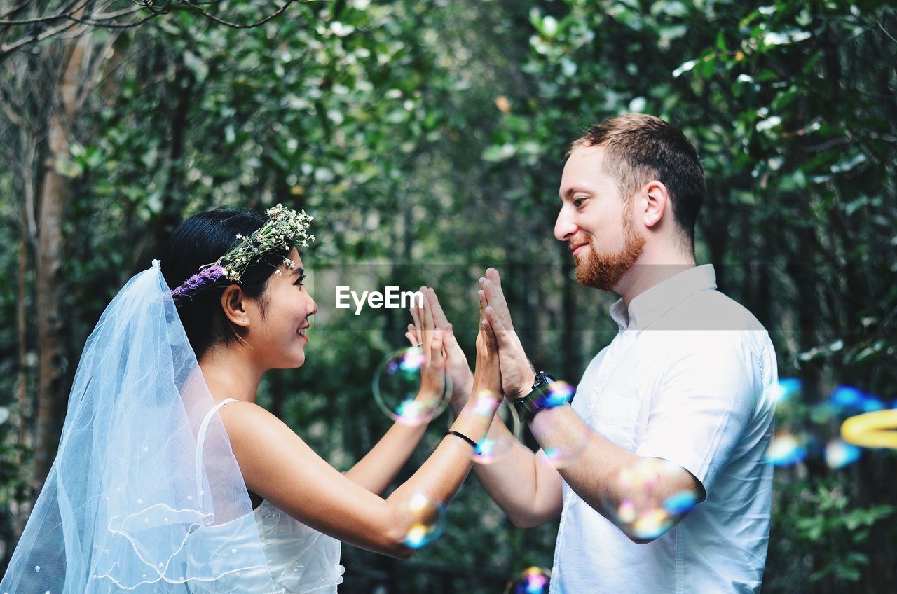 Side view of couple holding hands while standing against trees in park