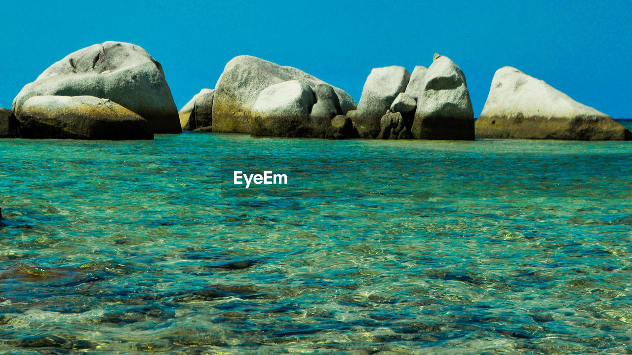 Rock formations in sea against clear blue sky