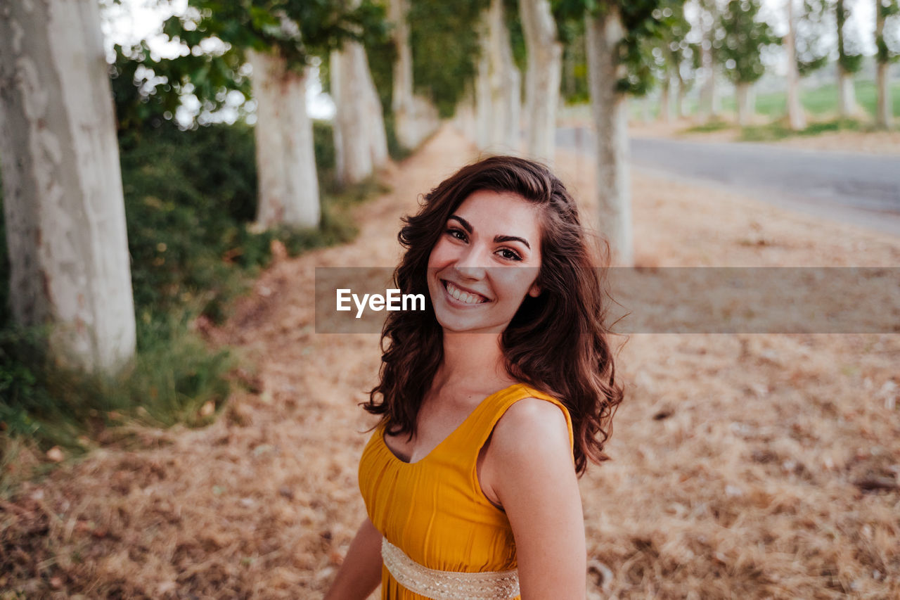 Portrait of smiling young woman against trees