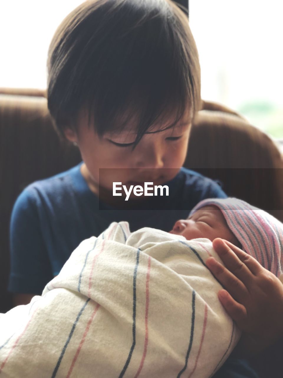 Cute boy carrying wrapped baby girl at home