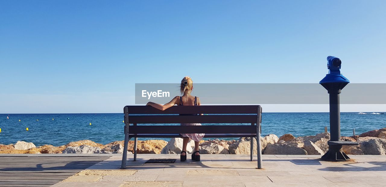 Rear view of woman sitting on bench by sea against sky