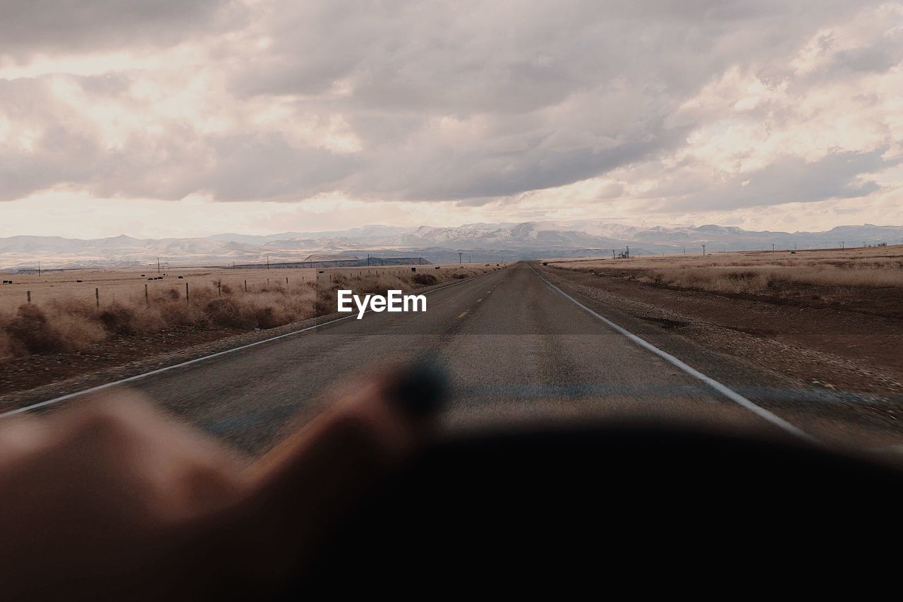 Cropped image of woman driving car while road seen through windshield