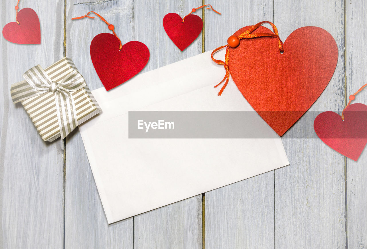 Directly above shot of heart shapes with blank paper and gift box on wooden table