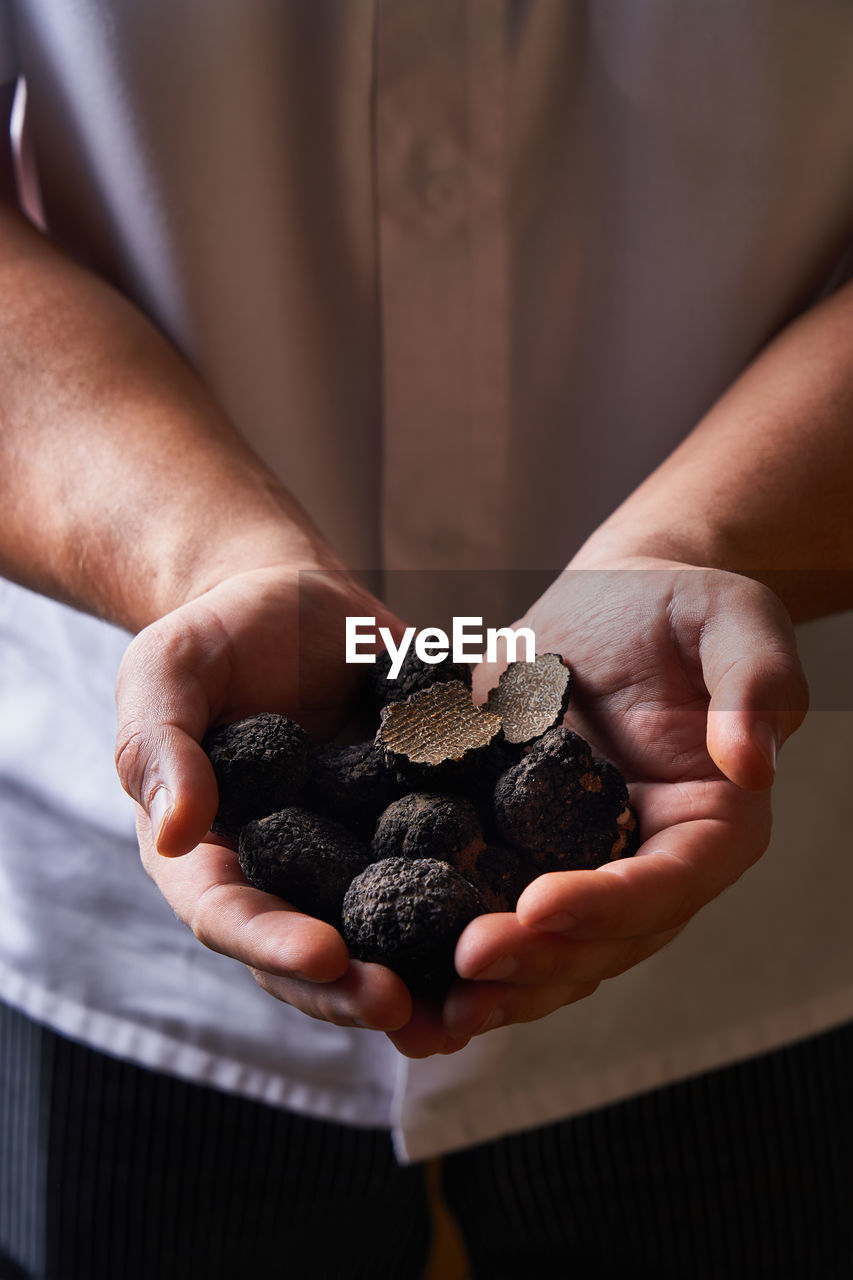 Unrecognizable cook demonstrating handful of black truffles for exquisite dish preparation
