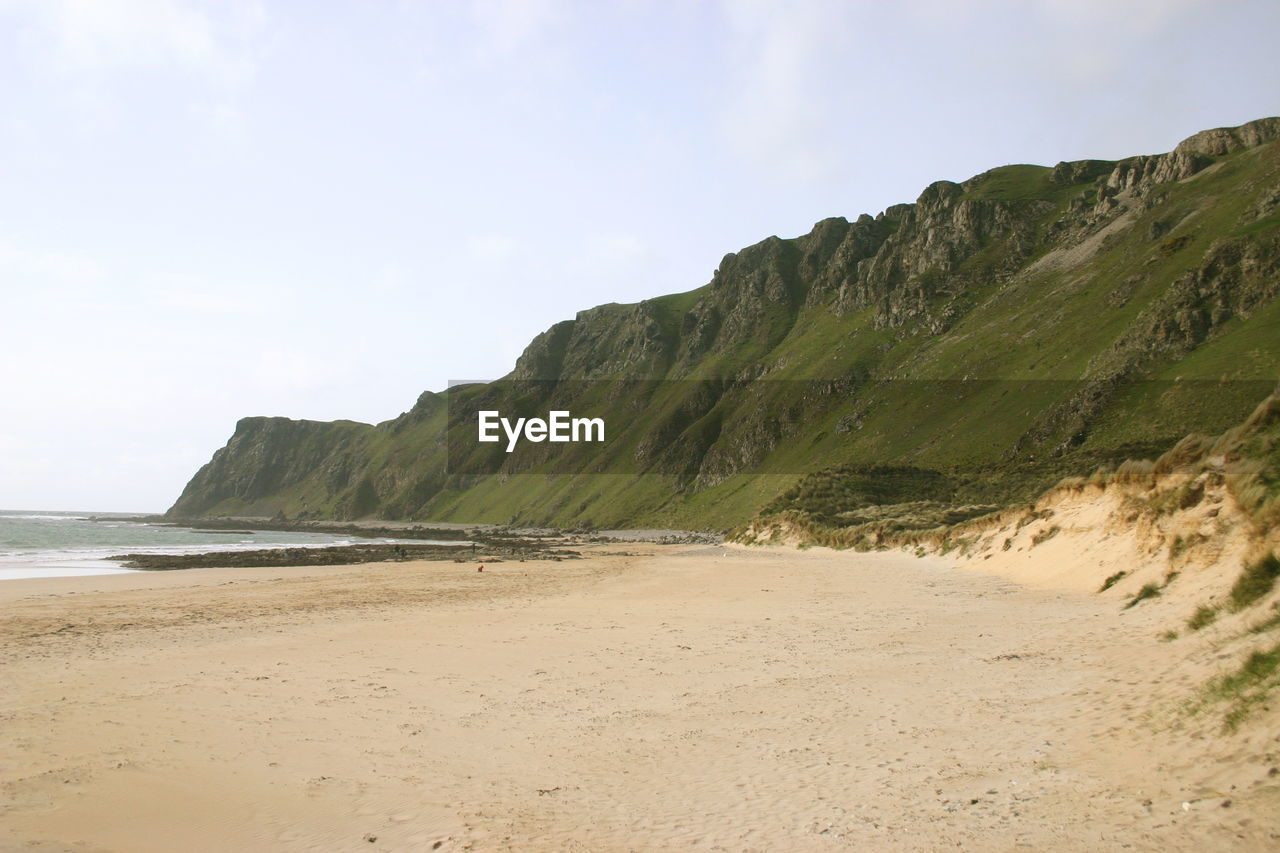 SCENIC VIEW OF BEACH BY MOUNTAIN AGAINST SKY