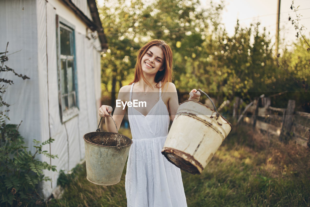 Smiling woman holding buckets while standing outdoors