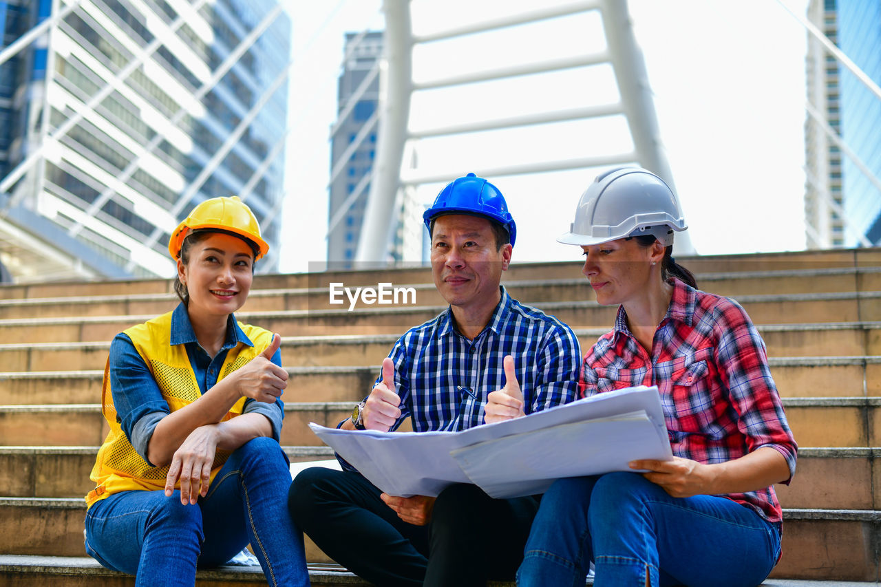 People working with blueprints while sitting on staircase