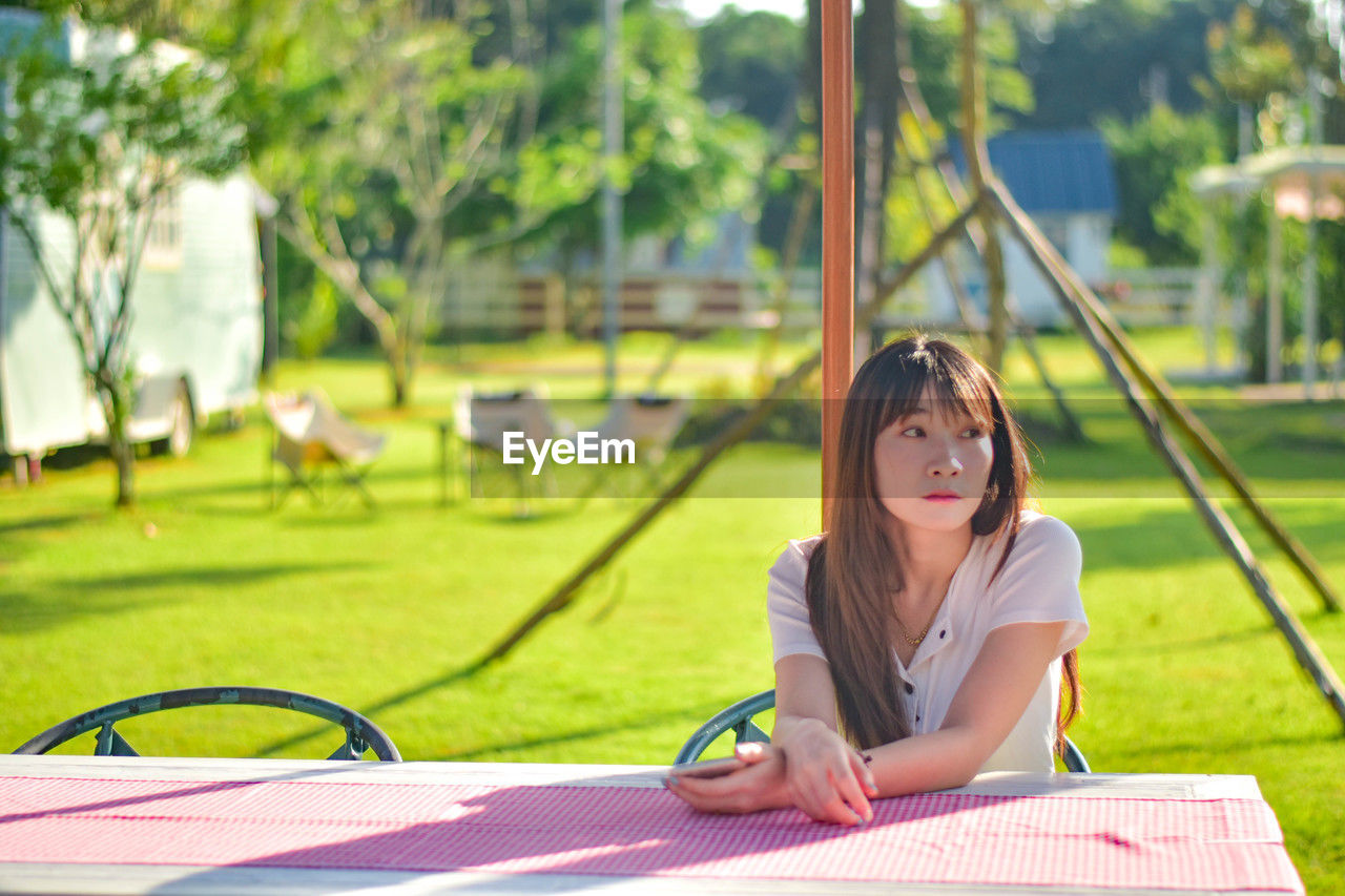 young woman reading book while sitting on swing at park