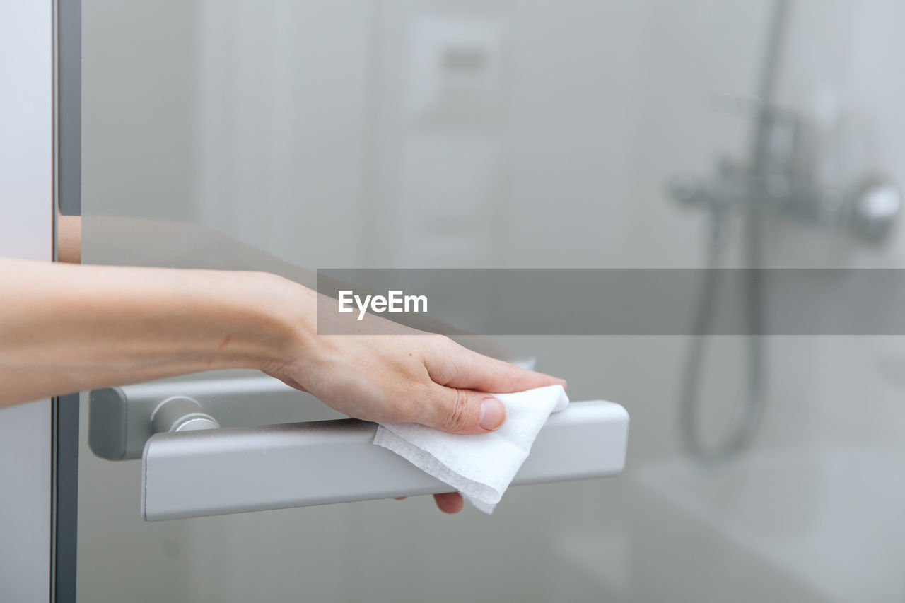 Cleaning glass door handles with an antiseptic wet wipe. woman hand using 