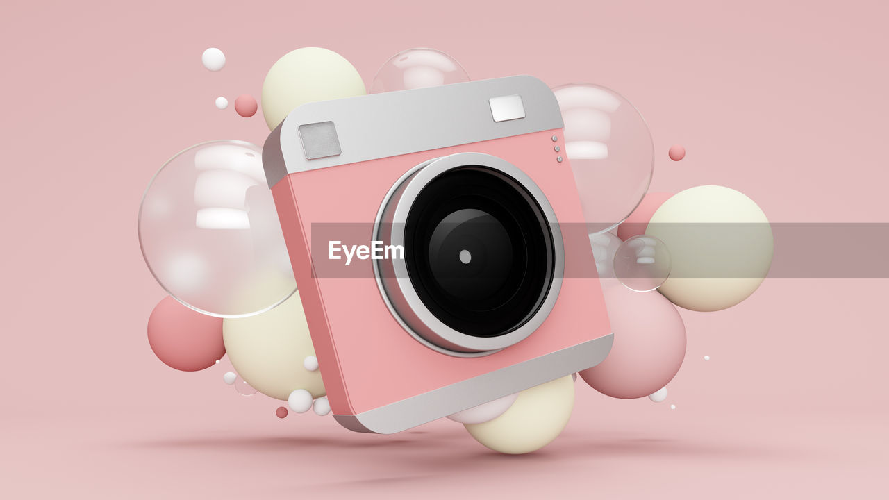 Three dimensional render of old-fashioned camera floating with various bubbles against pink background