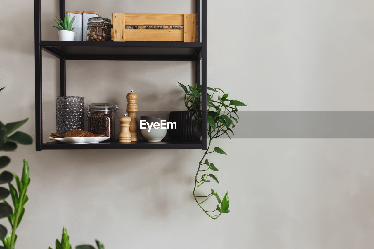 Black metal shelves in the kitchen on a gray concrete wall in a loft style. green flowerpots