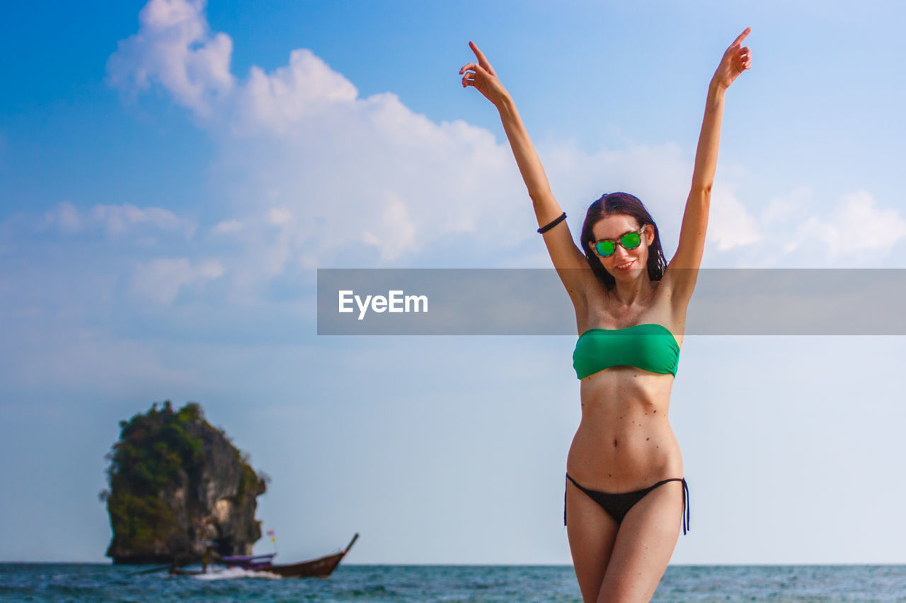 Carefree woman wearing bikini standing at beach against sky