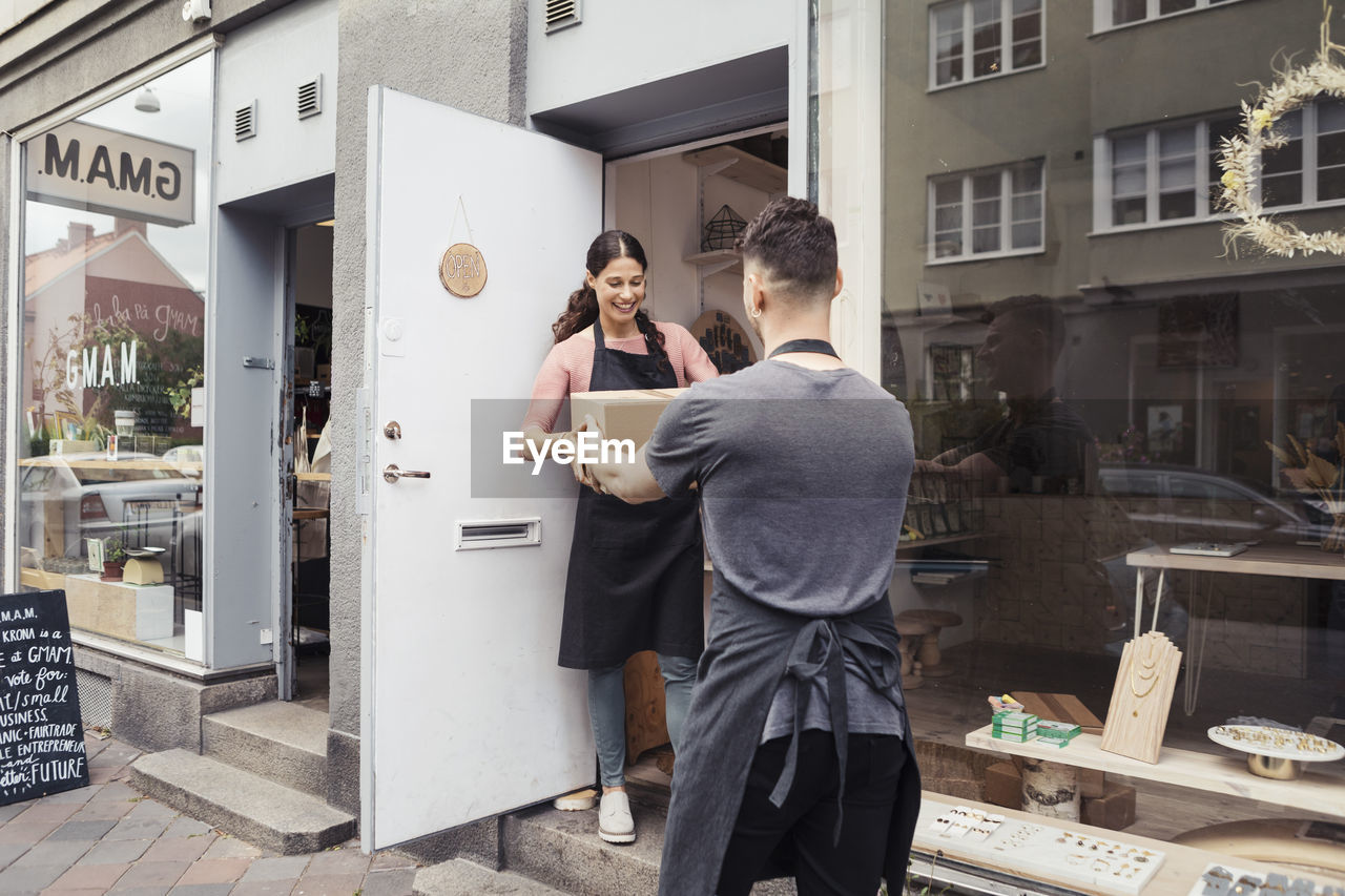 Male owner giving package box to female colleague outside design studio