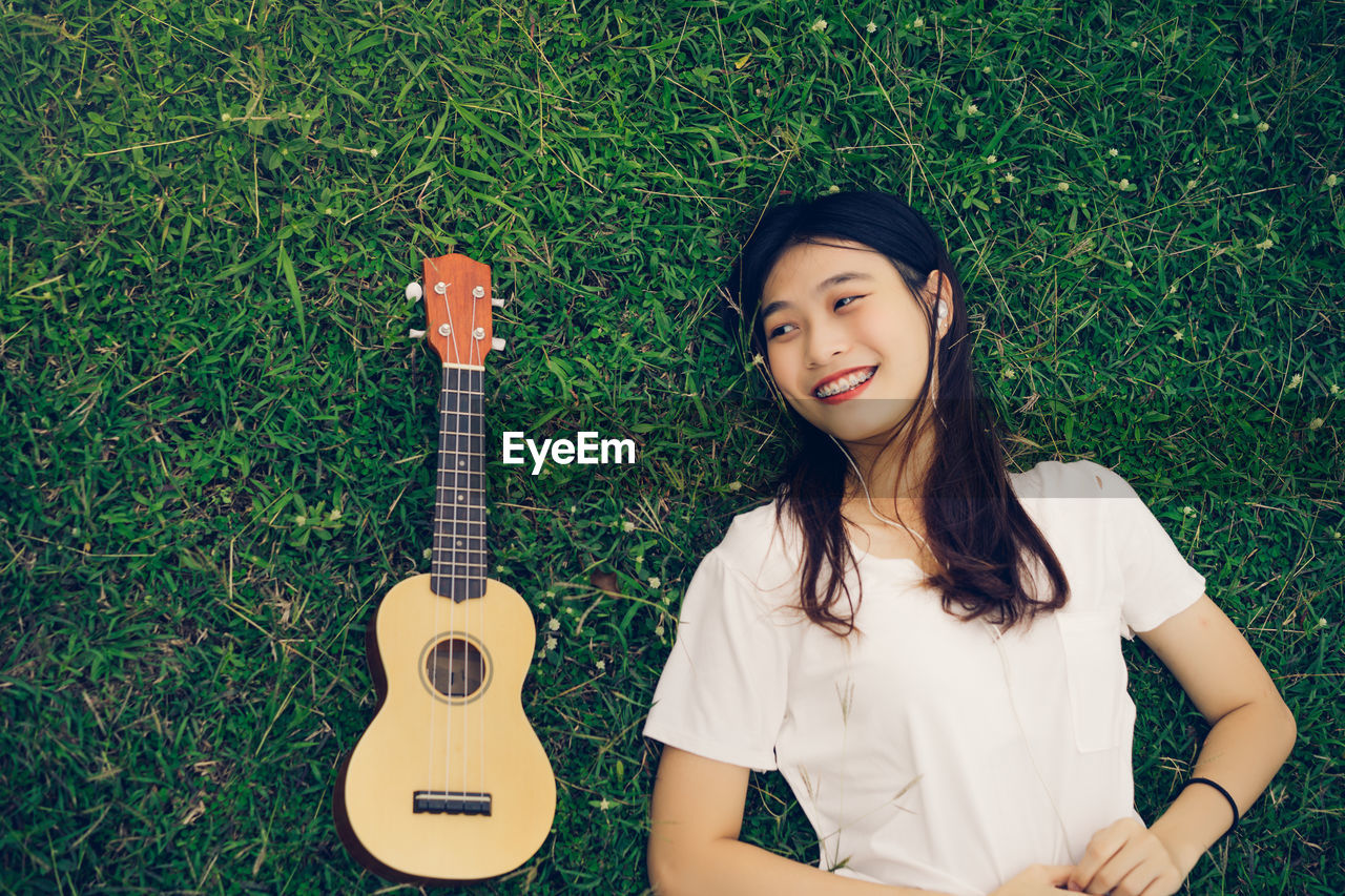 Smiling young woman listening music by ukulele on grass
