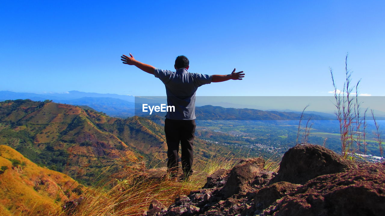 Man standing with arms outstretched standing on mountain against blue sky