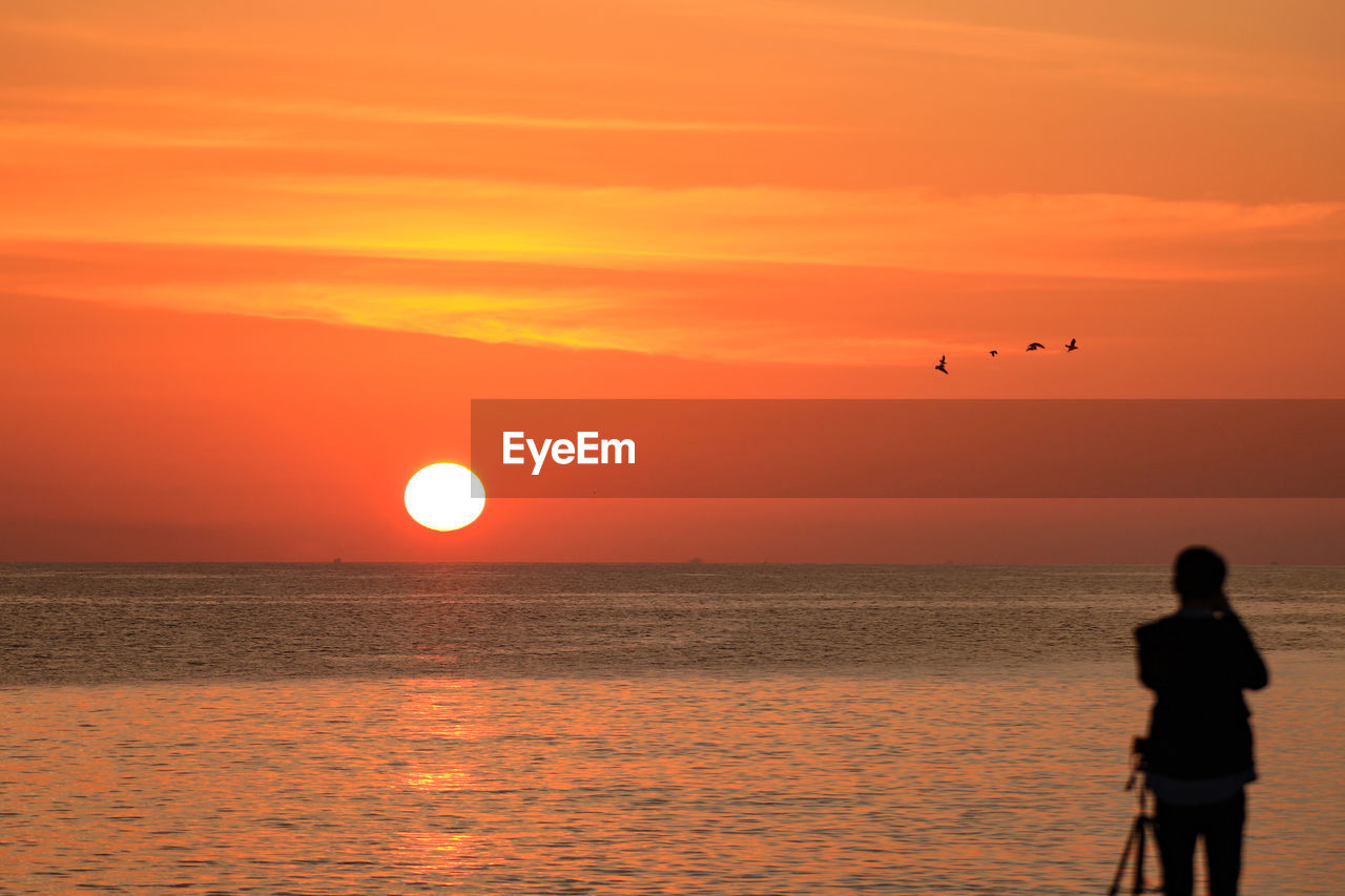 Silhouette man standing on beach against orange sky