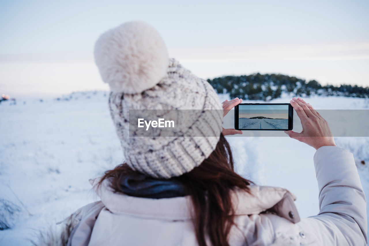 Backpacker woman hiking in snowy mountain taking a picture with mobile phone.winter season