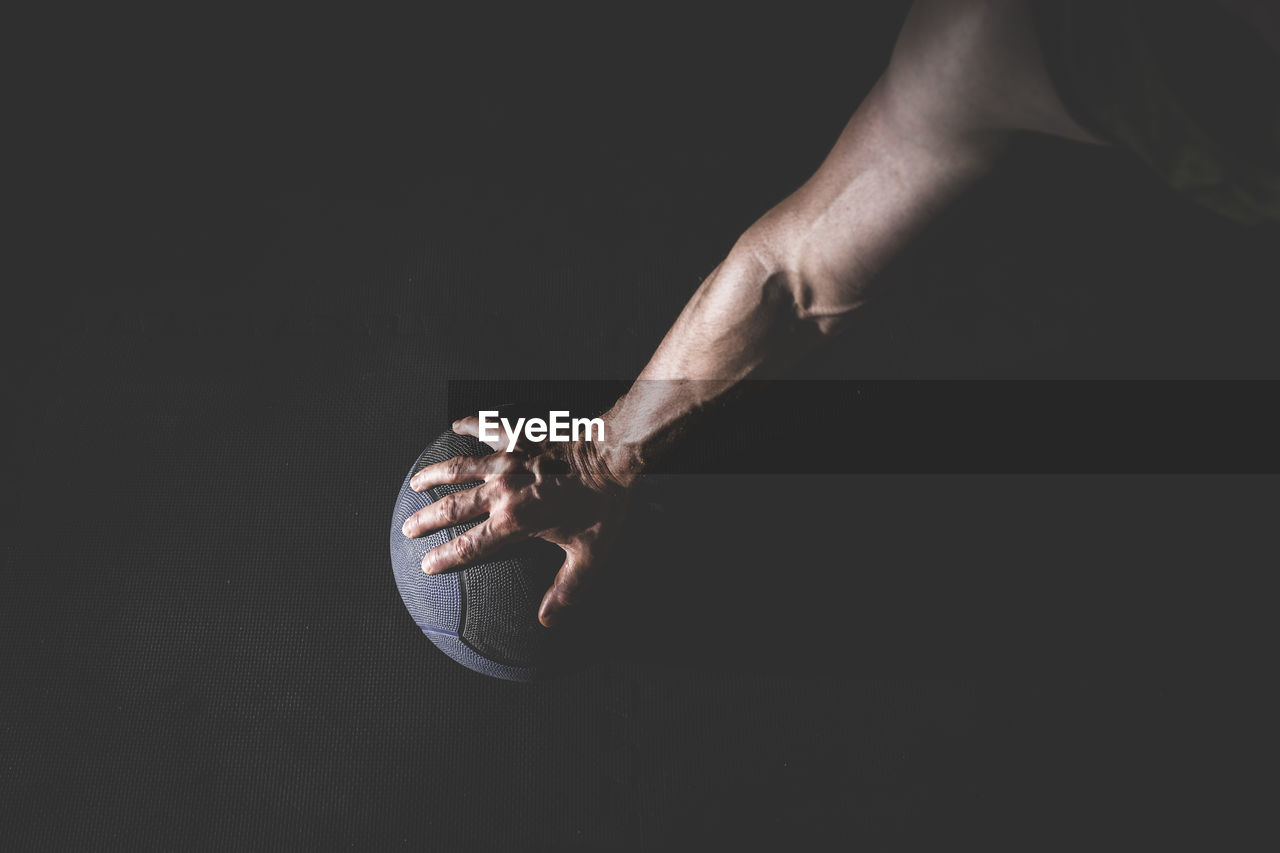 Close-up of hand holding basketball over black background