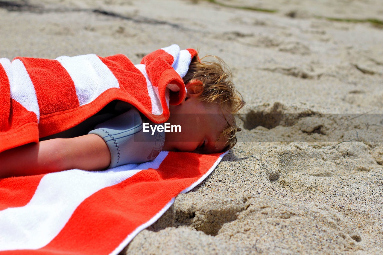 Boy with towel sleeping at beach on sunny day