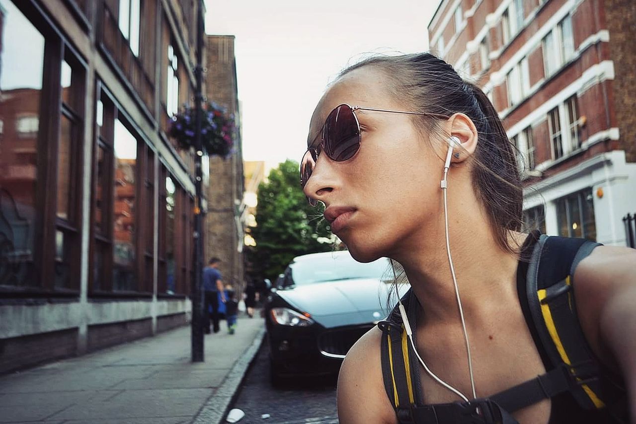 Thoughtful beautiful woman looking away while listening to music in city