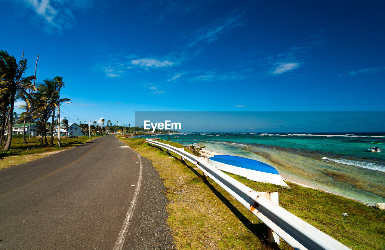 Empty road by sea against blue sky