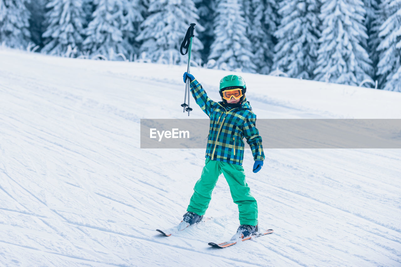 Full length portrait of boy holding ski poles on snow covered land