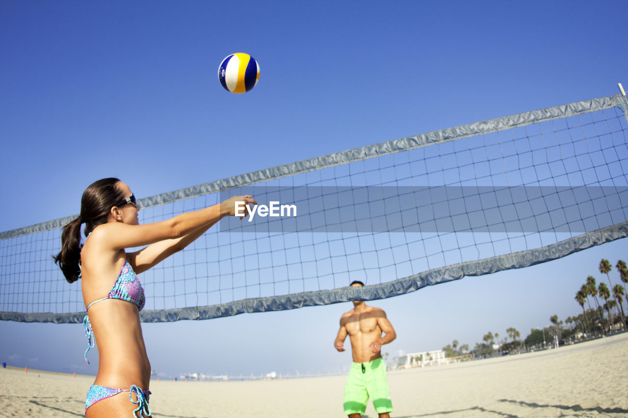 Couple playing beach volleyball against clear sky