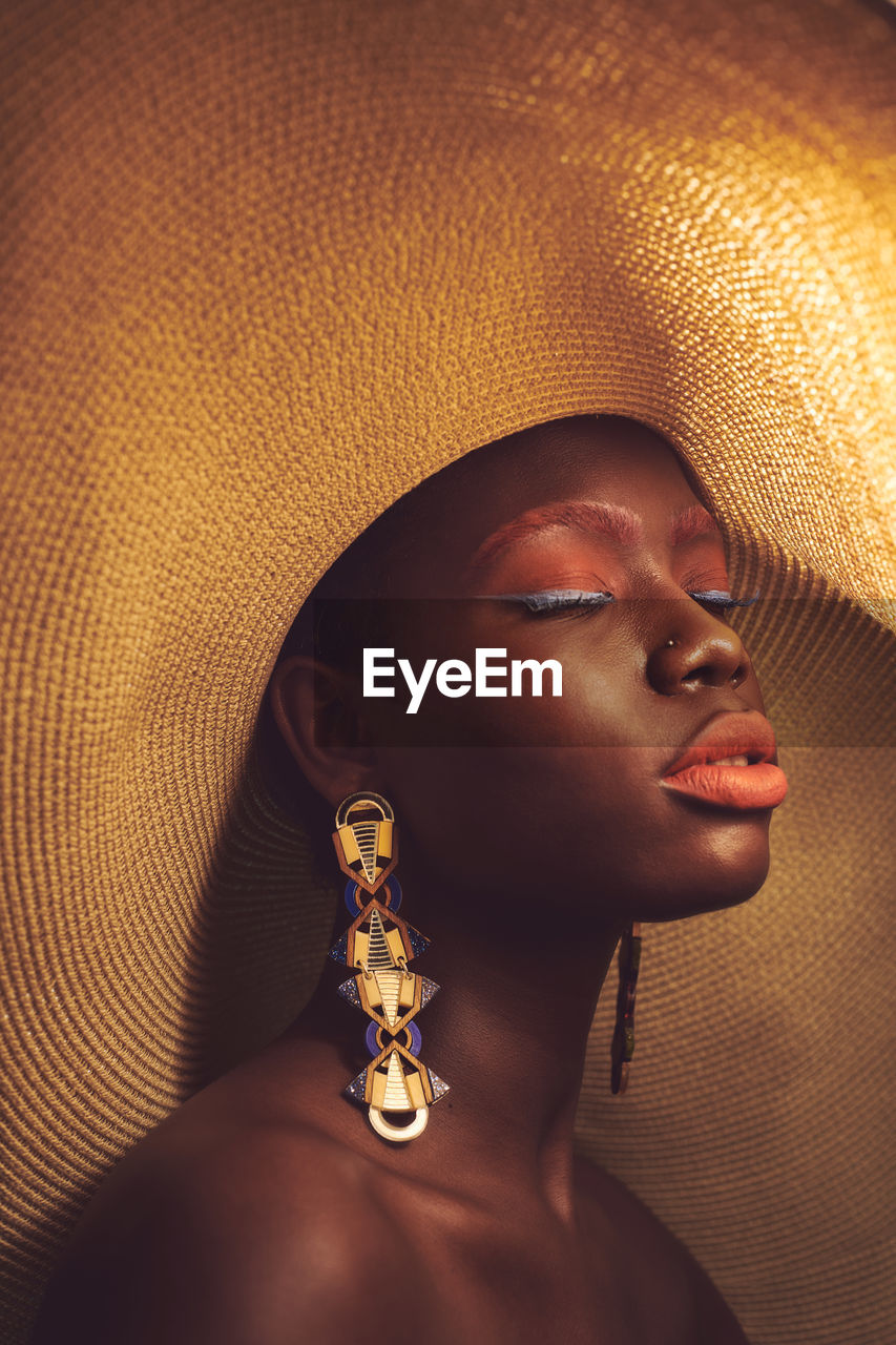 Black woman in large sun hat and statement earrings with eyes closed 
