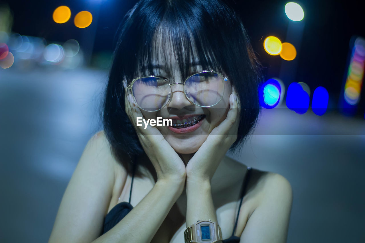 Portrait of smiling woman with hands on chin standing outdoors at night