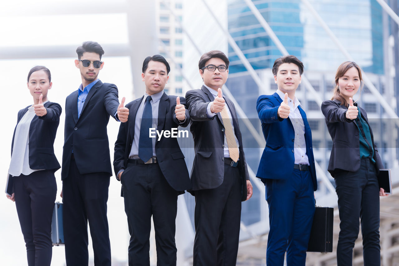Portrait of businesspeople showing thumbs up against buildings in city