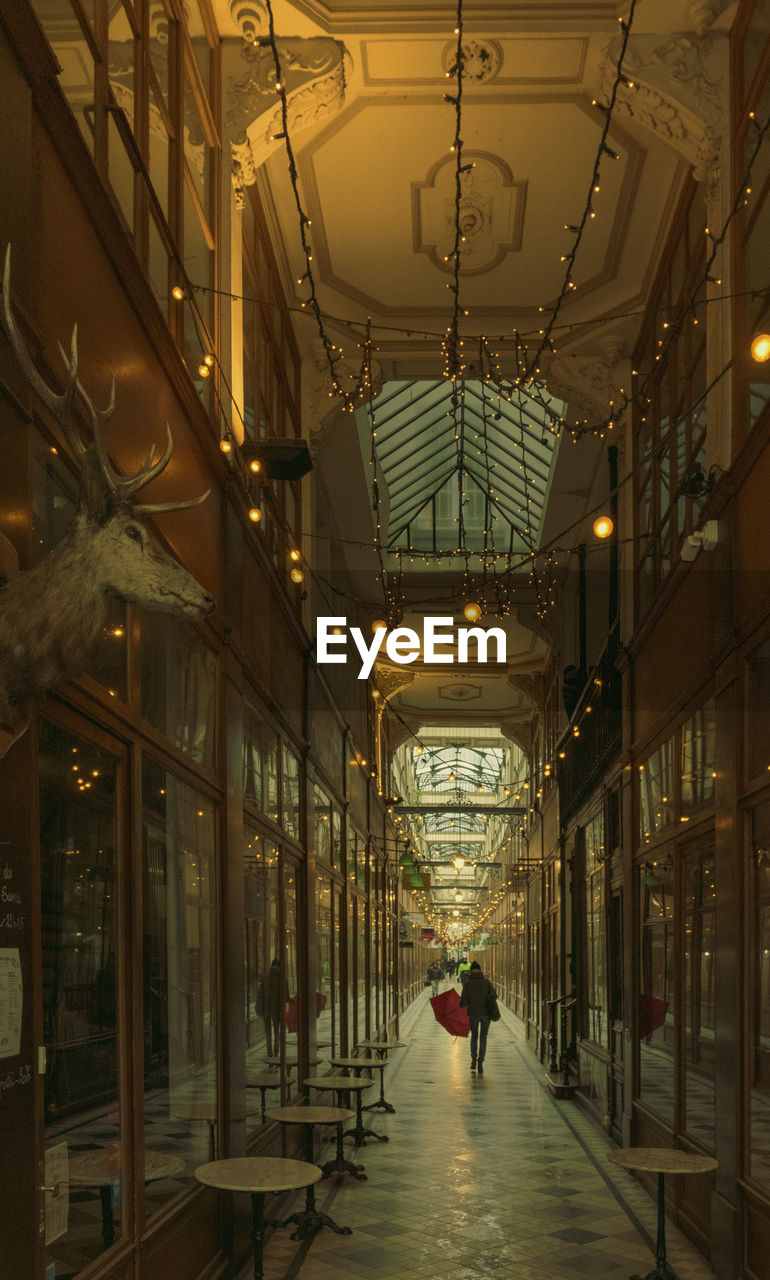 REAR VIEW OF PEOPLE WALKING IN ILLUMINATED CORRIDOR OF BUILDING