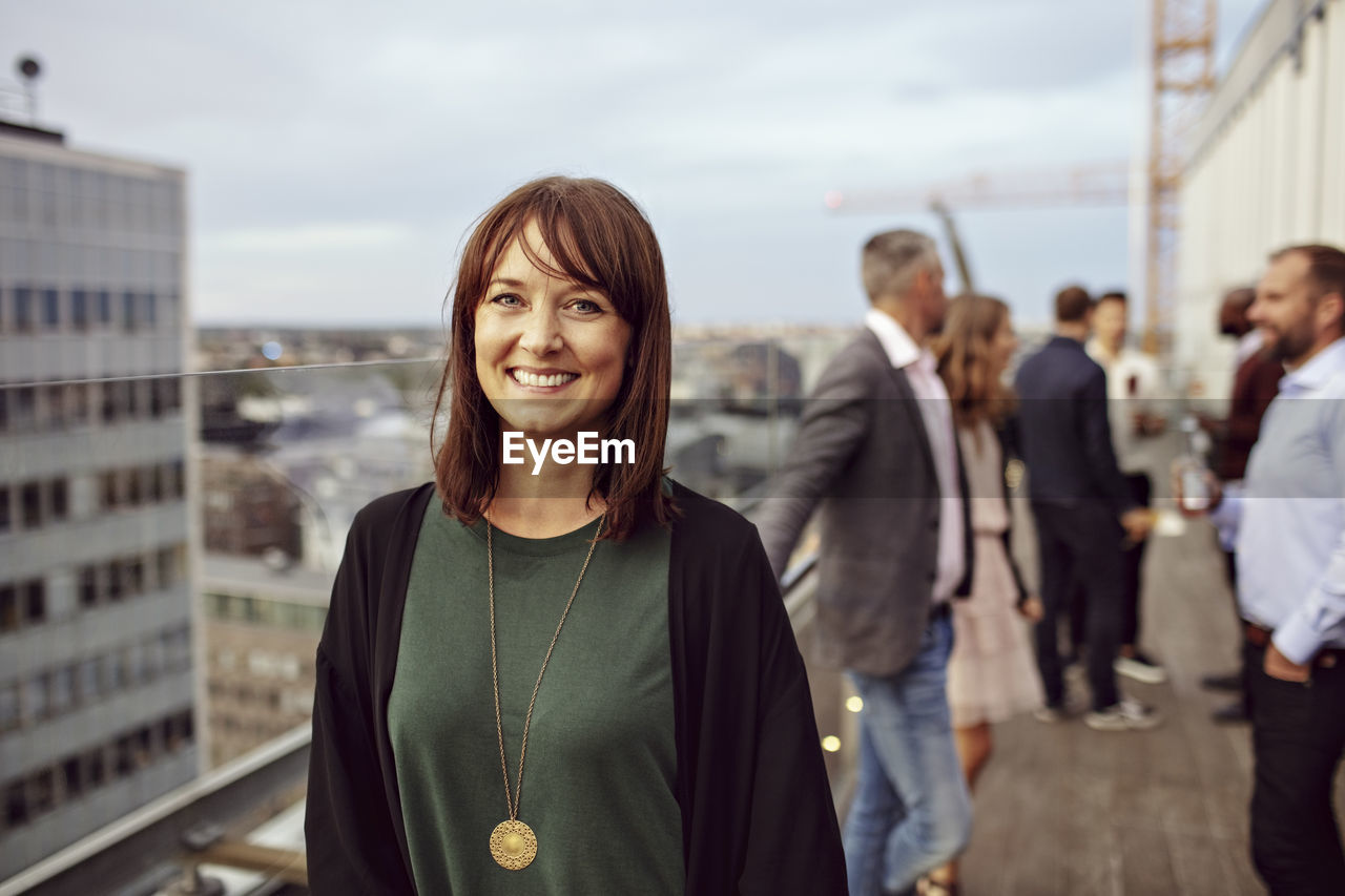 Portrait of smiling businesswoman with colleagues in background standing on terrace during party