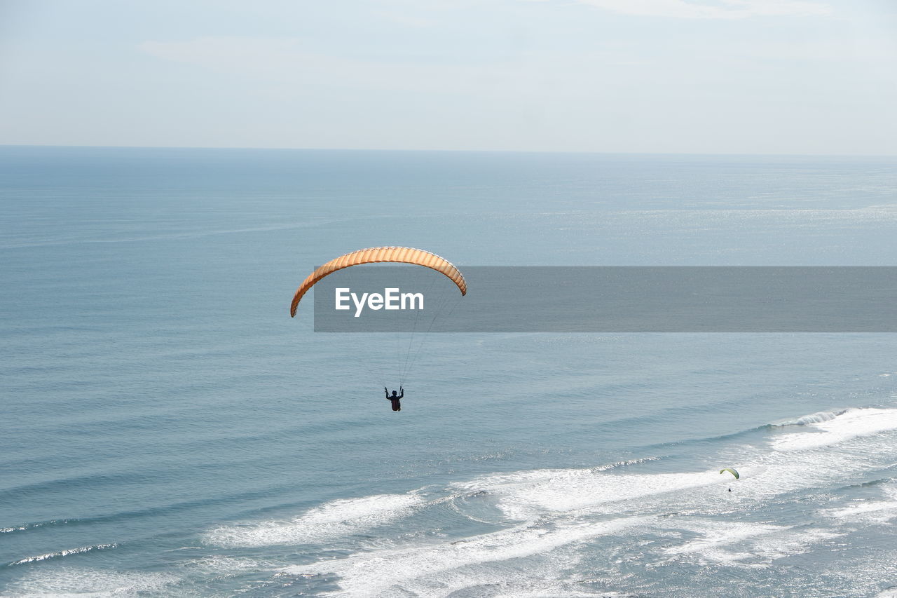 PEOPLE FLYING KITE BY SEA AGAINST SKY