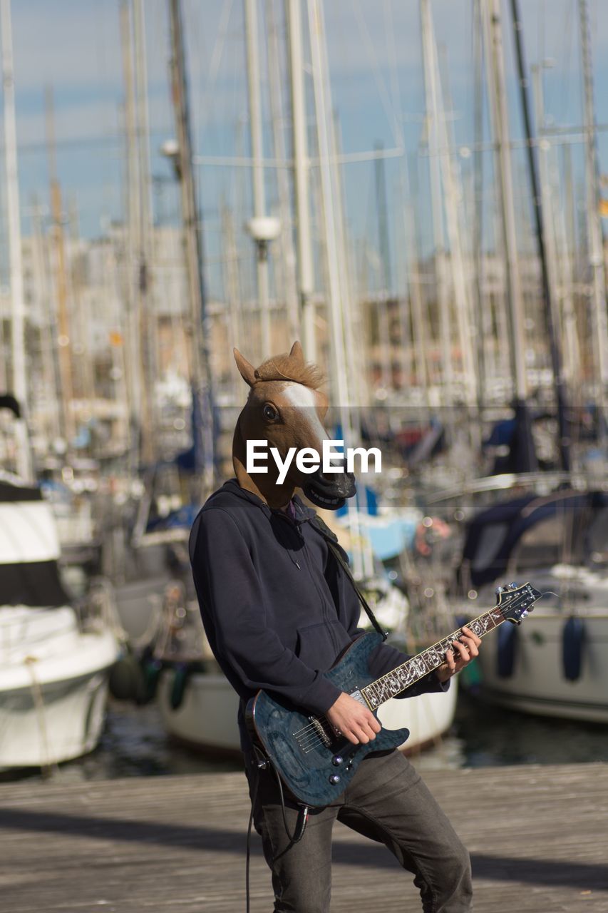 Man wearing horse mask while playing guitar at harbor