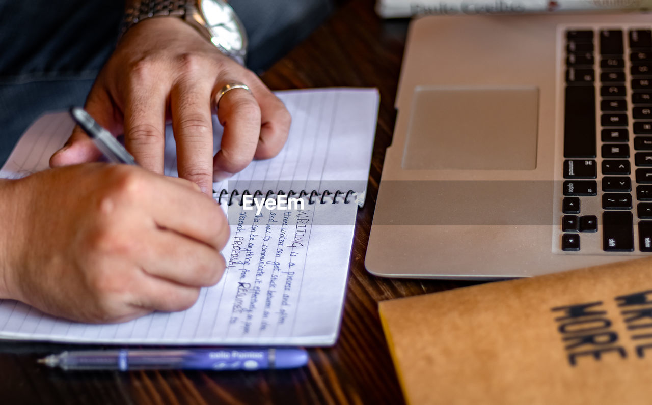 Close-up of man writing in book on table
