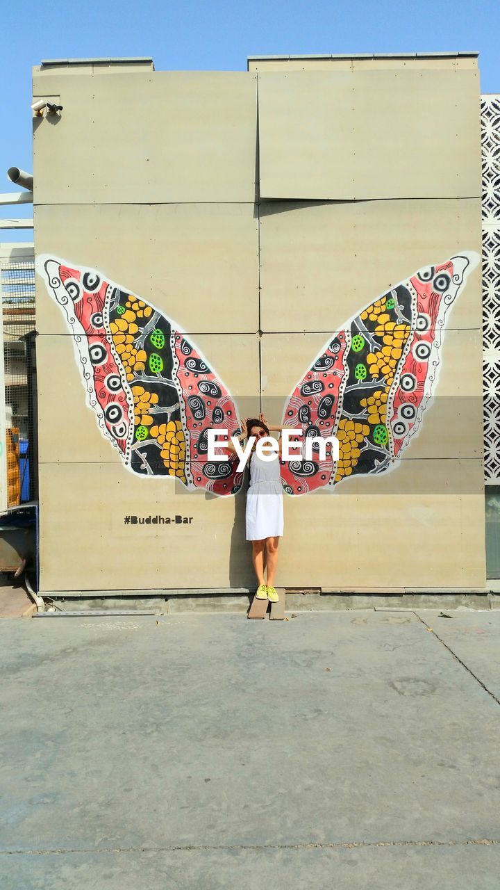 REAR VIEW OF WOMAN STANDING AGAINST MULTI COLORED WALL