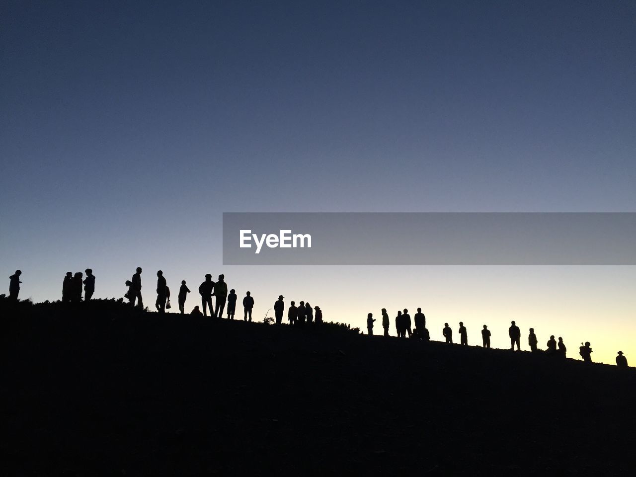 Silhouette people standing on field against clear blue sky during sunset