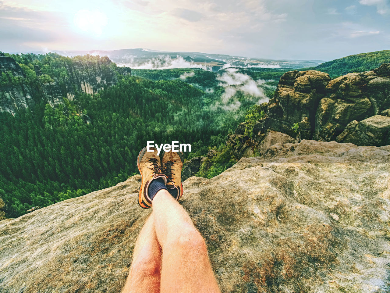 Hiker man take a rest on mountain peak. male legs on sharp summit and hiker enjoy spectacular view.