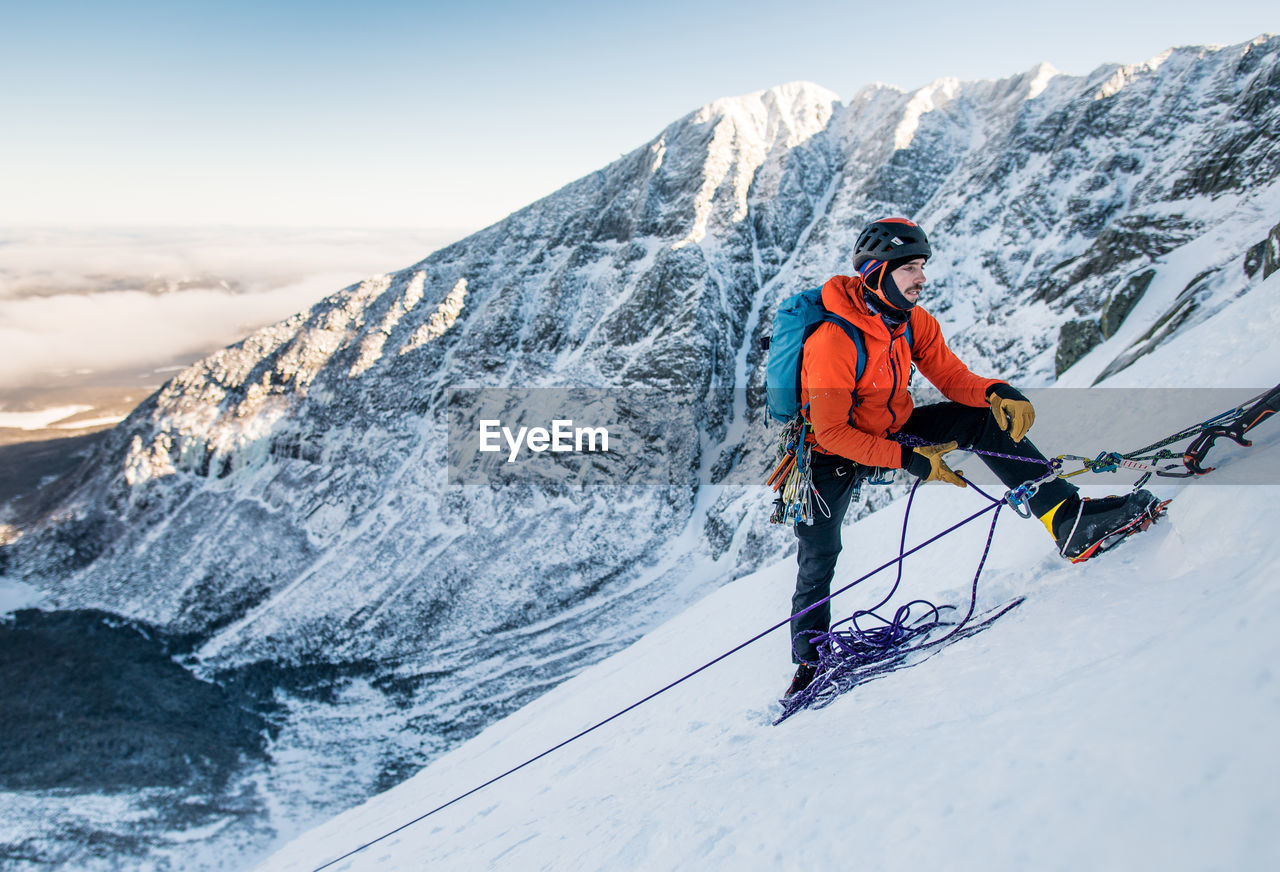 A male climber belays another climber during a winter alpine ice climb