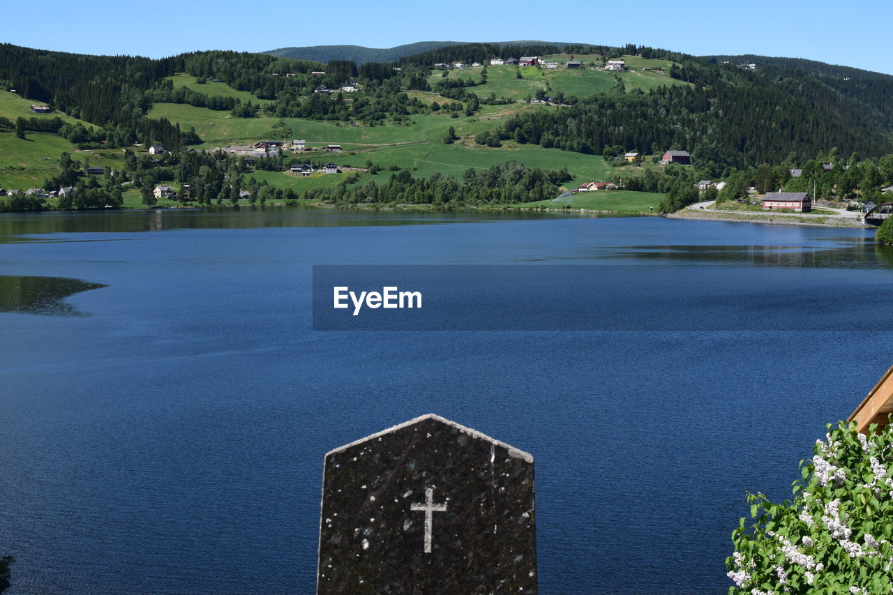 Scenic view of lake by buildings against sky with gravestone in fore front.