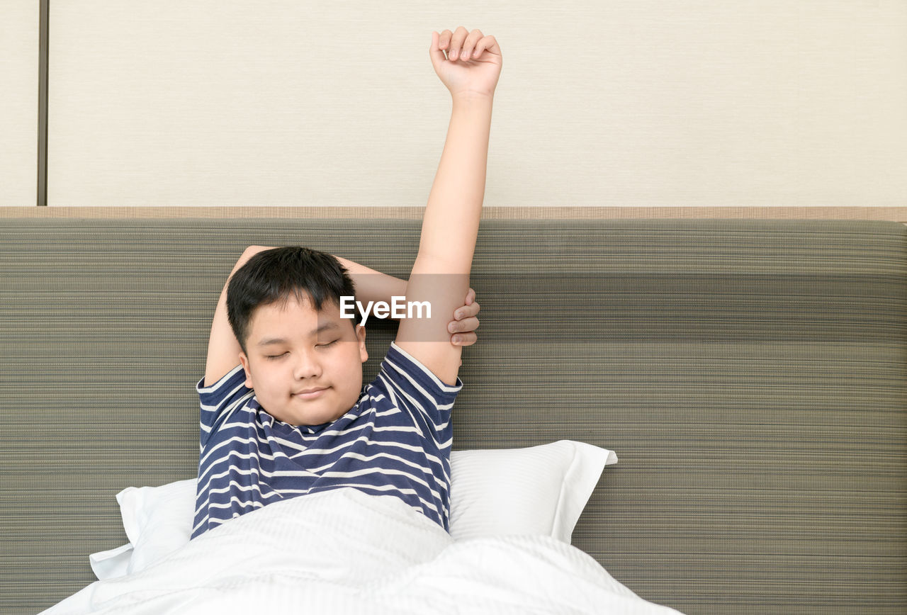 Obese fat boy wakes up and stretching on bed in morning,