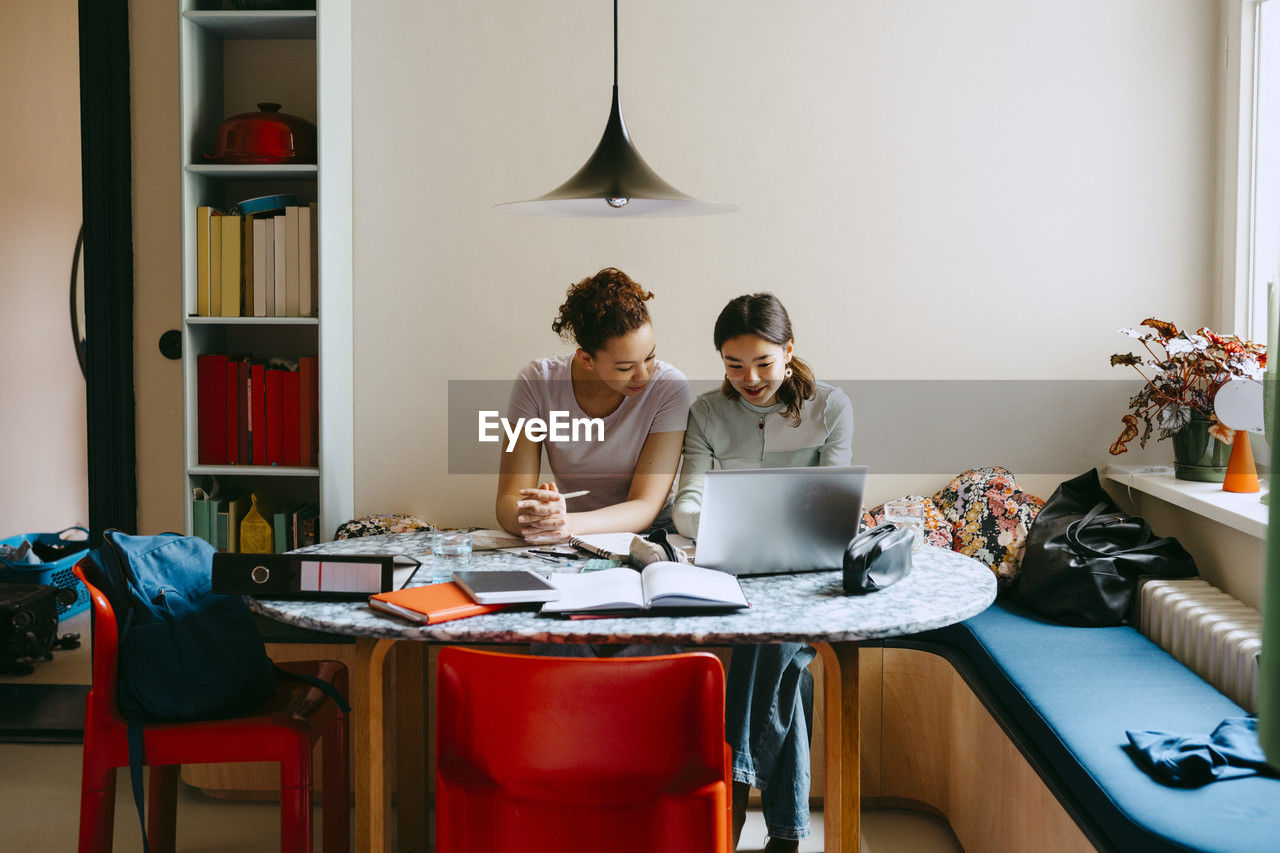 Female friends studying together while using laptop at table