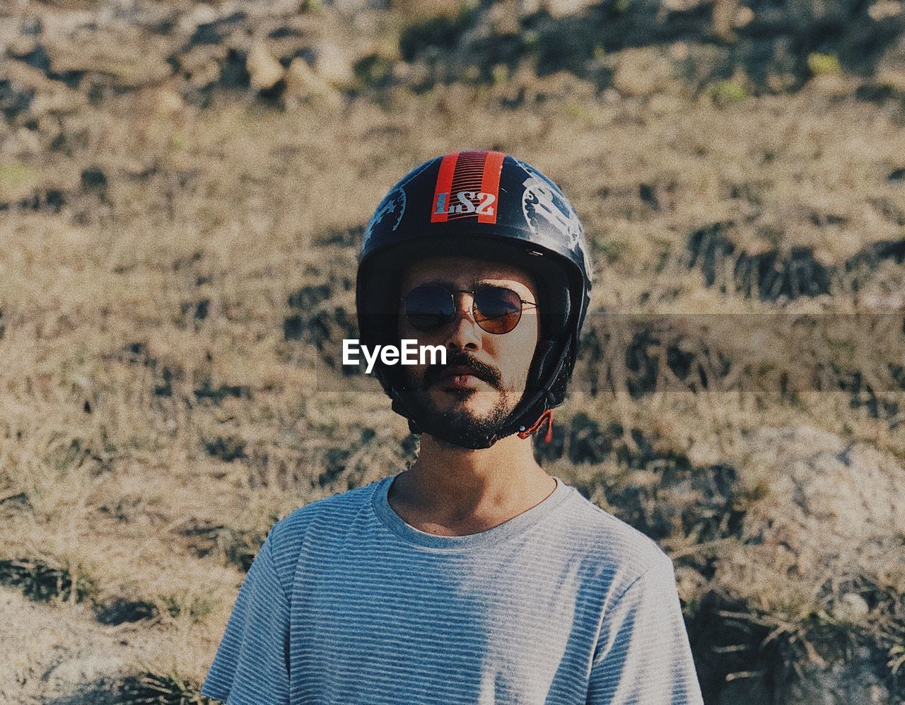 Portrait of young man wearing sunglasses and helmet while standing against hill during sunny day