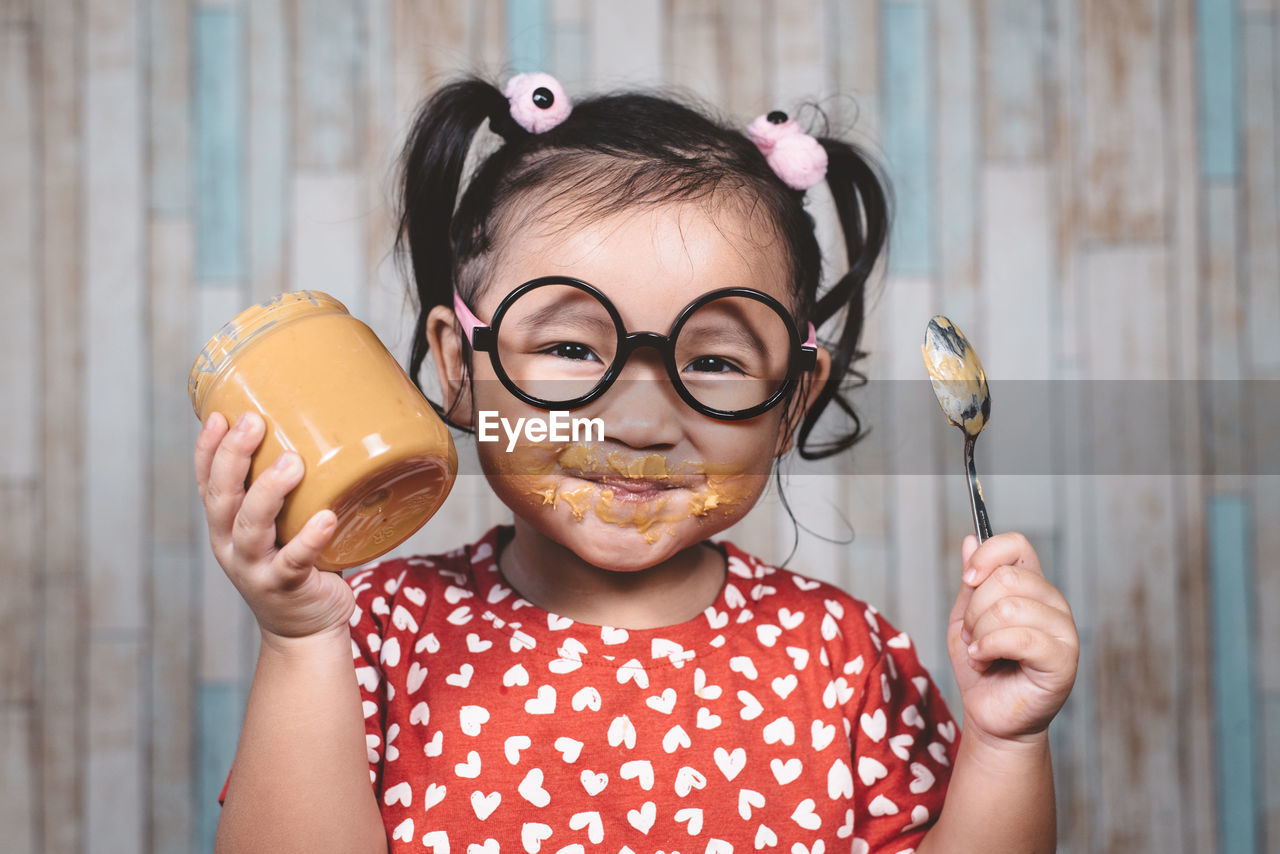 Portrait of happy girl holding spoon and peanut butter bottle