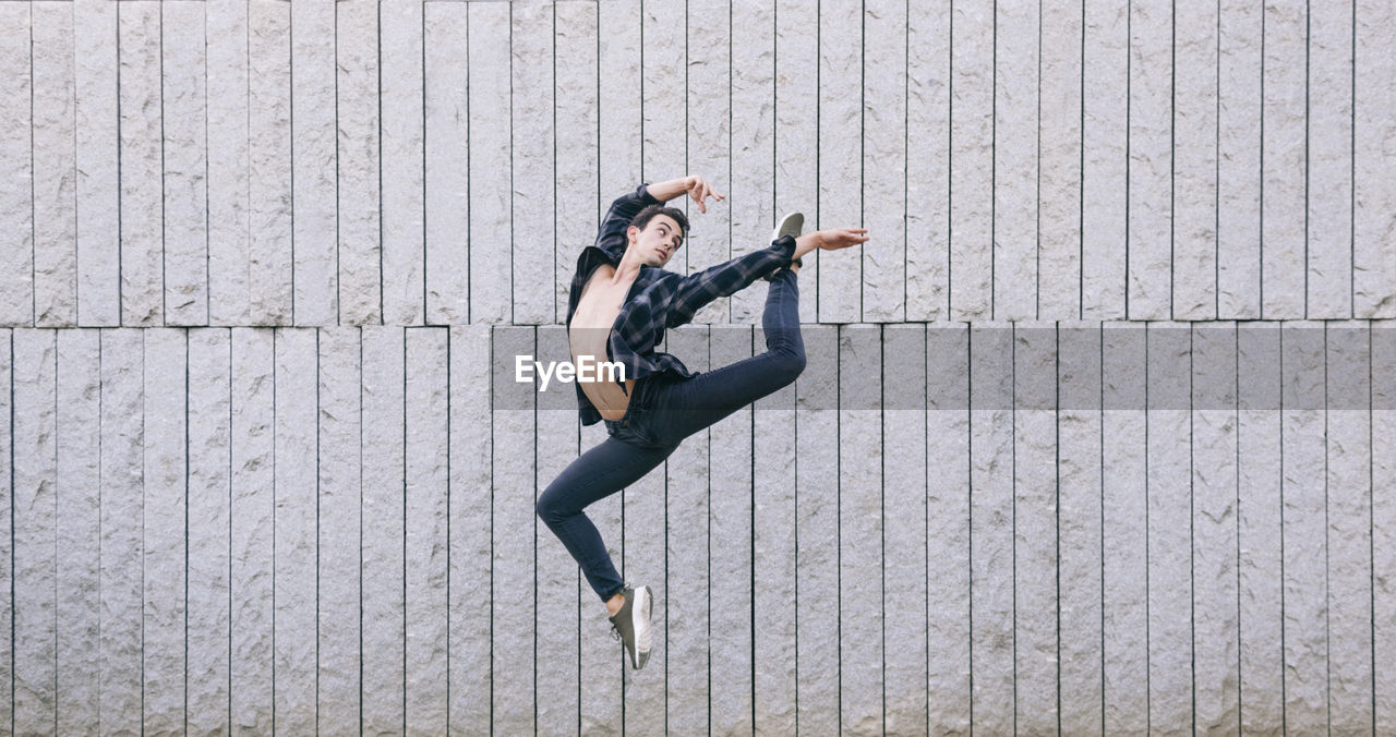 Full length of man jumping while dancing against wall