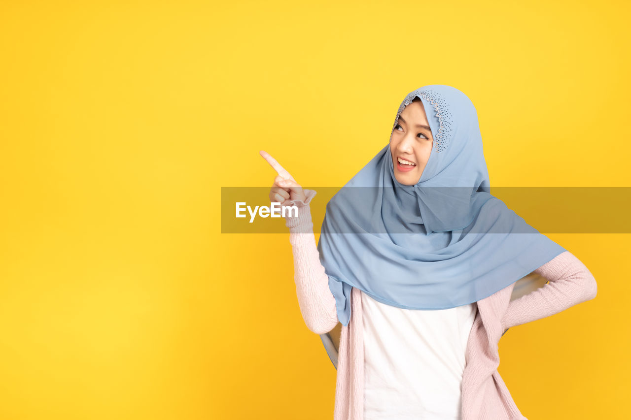 WOMAN STANDING AGAINST YELLOW BACKGROUND